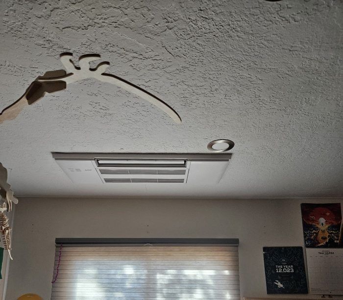 Person holding a wooden cutout toward a textured ceiling with a recessed light and vent.