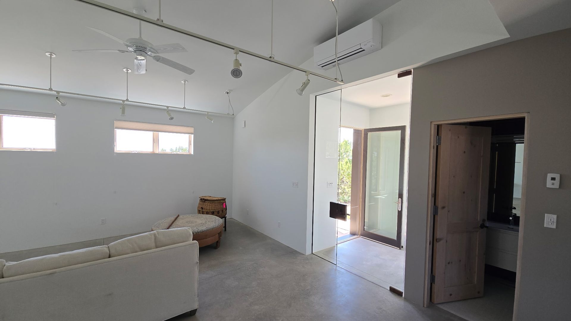 A bright living area with white walls, a sofa, and an open glass doorway.