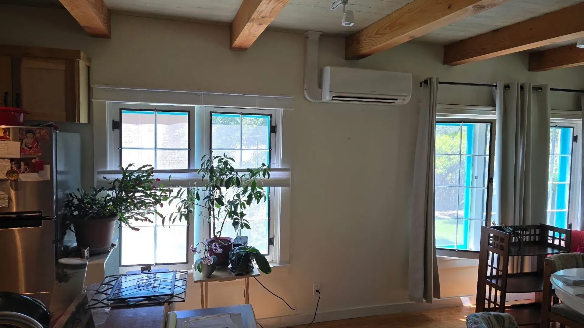 Interior view of a room with windows, plants, air conditioning, and wood beams on the ceiling.