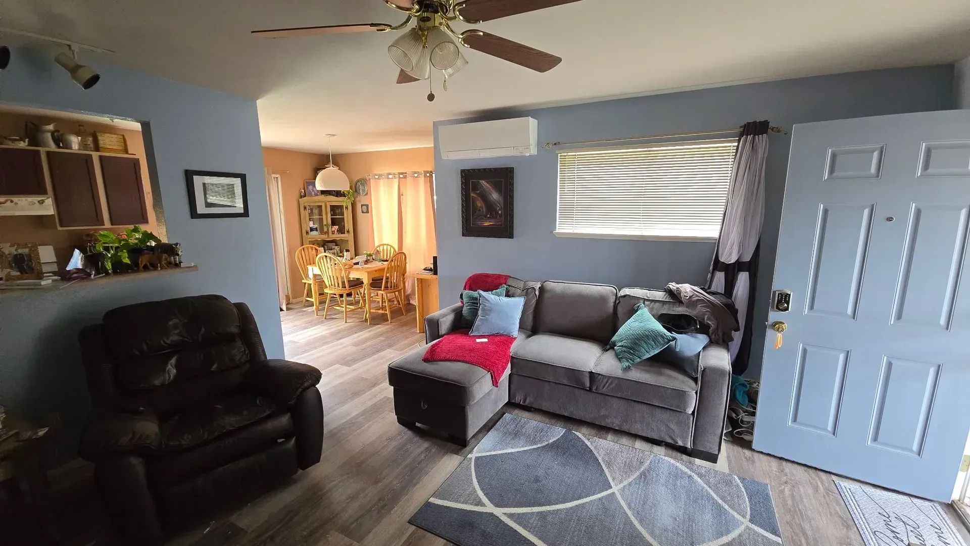 Cozy living room with blue walls, gray couch, armchair, and open doorway to dining area.