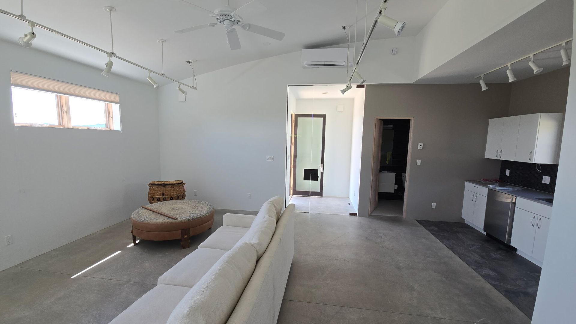 Man in red shirt stands with arms crossed under a wall-mounted Mitsubishi AC unit over a doorway.