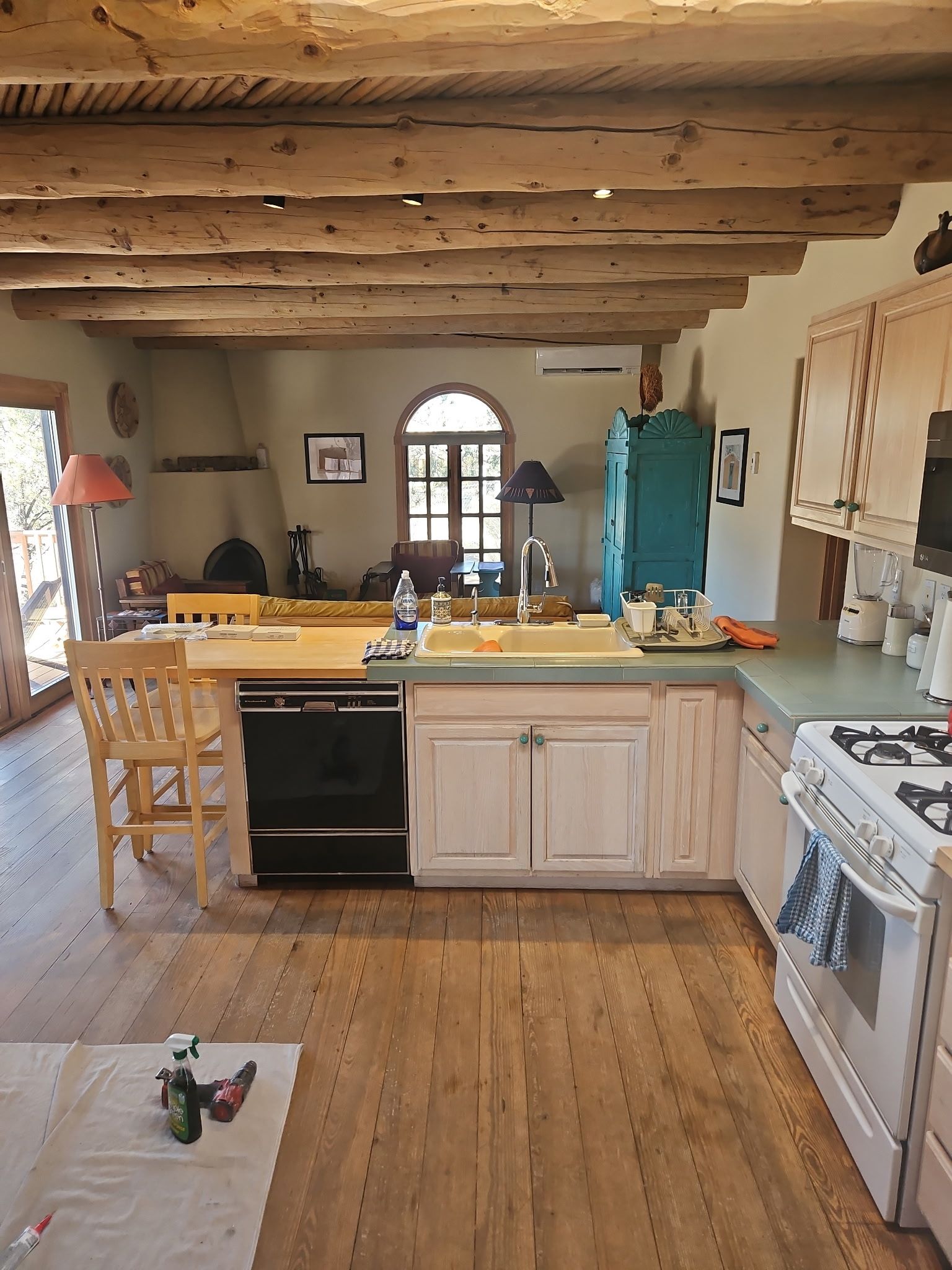Kitchen with wooden beams, light cabinets, and a turquoise cabinet. A door is visible in the background.
