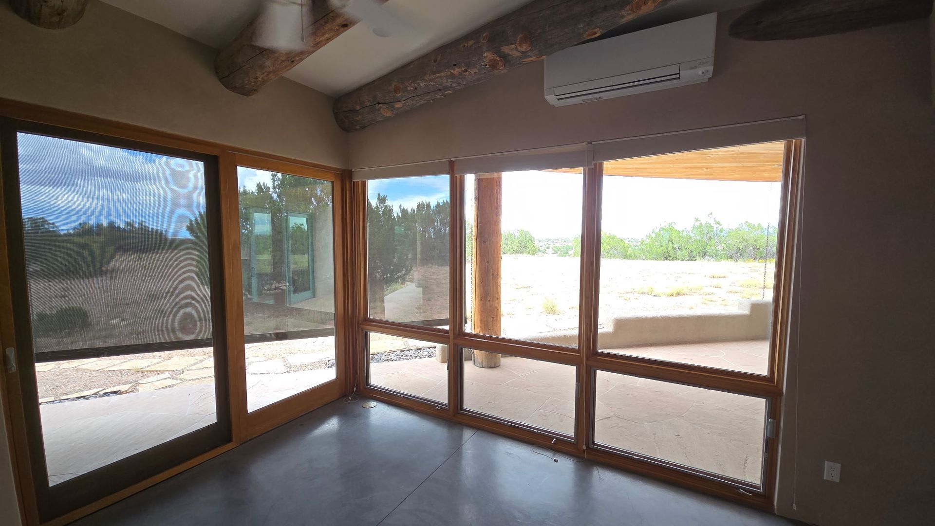 Room with large windows and sliding glass doors; view of an outdoor patio and trees.