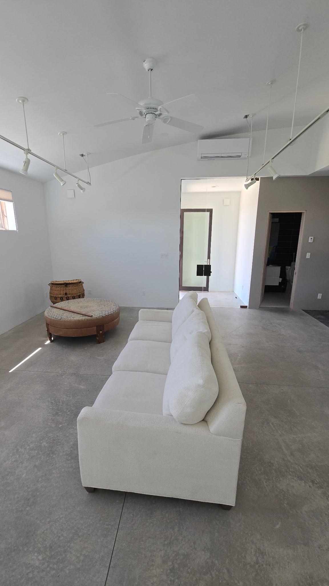 Spacious, white-walled living room with a white sofa and a wooden chaise lounge.