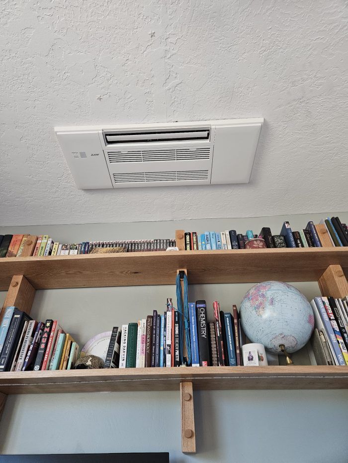 White ceiling-mounted air conditioning unit above a wooden bookshelf filled with books and a globe.