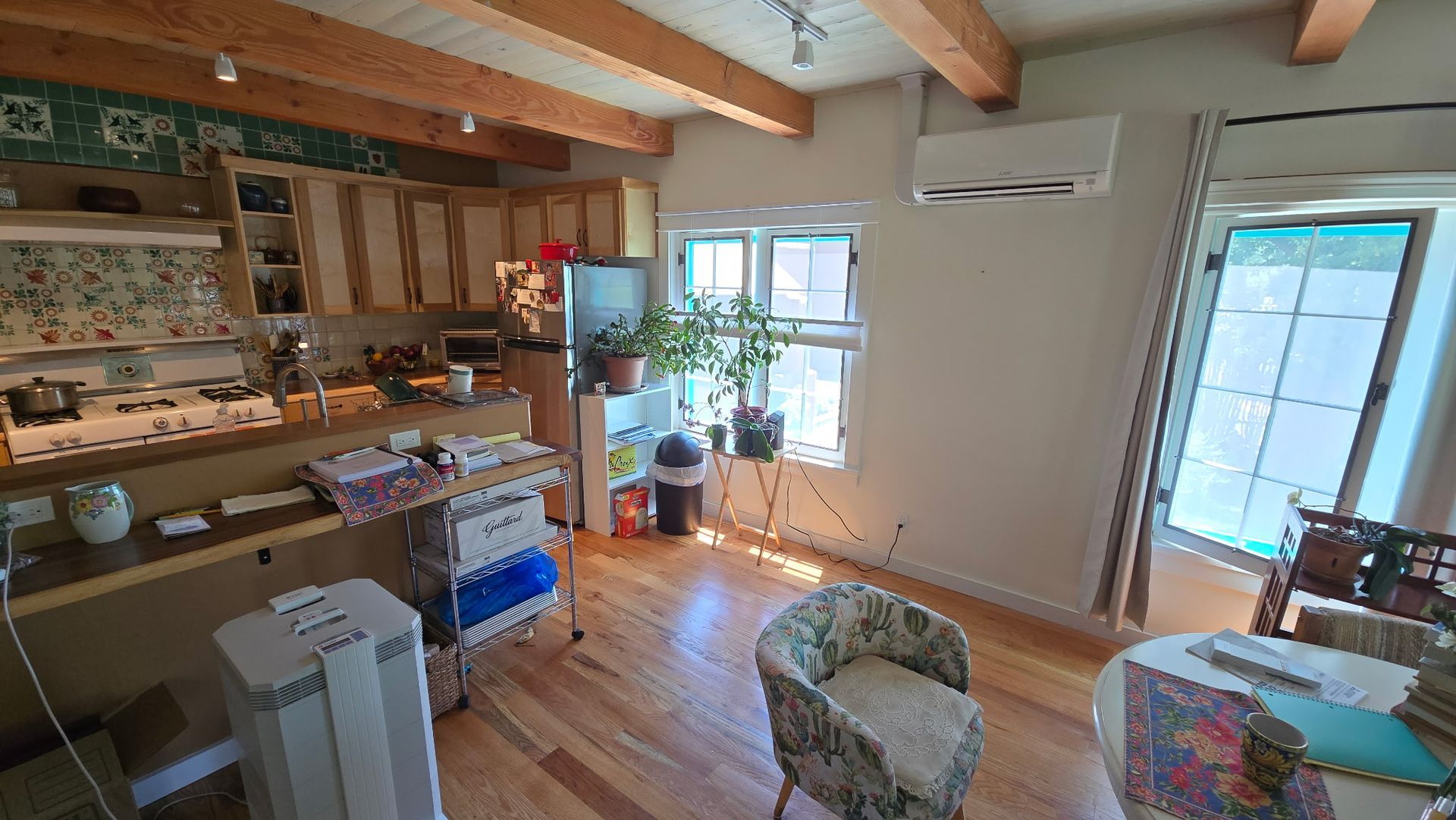 Kitchen and living area with wooden floors, light-colored cabinets, windows, and an air conditioner unit.