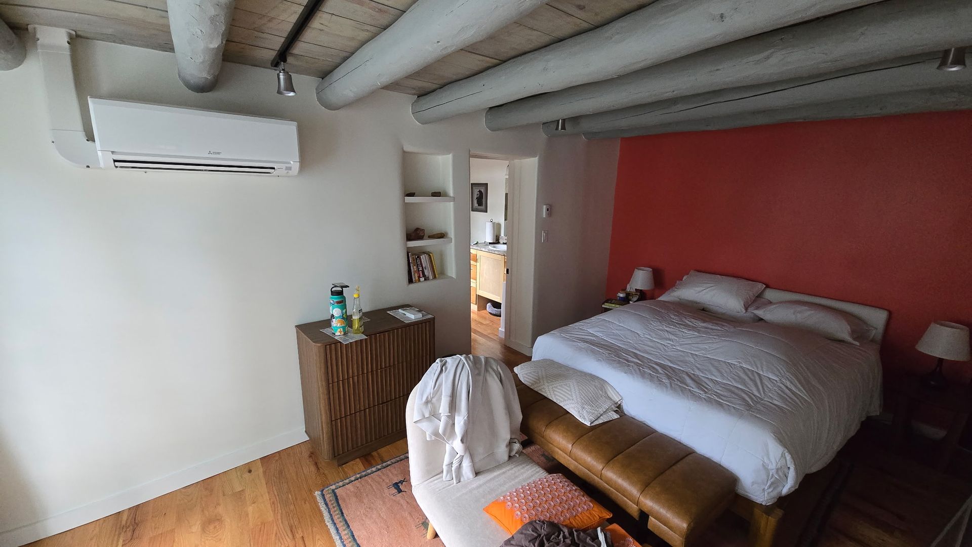 Bedroom with white walls, red accent wall, bed, wooden beams, and a small built-in shelf.