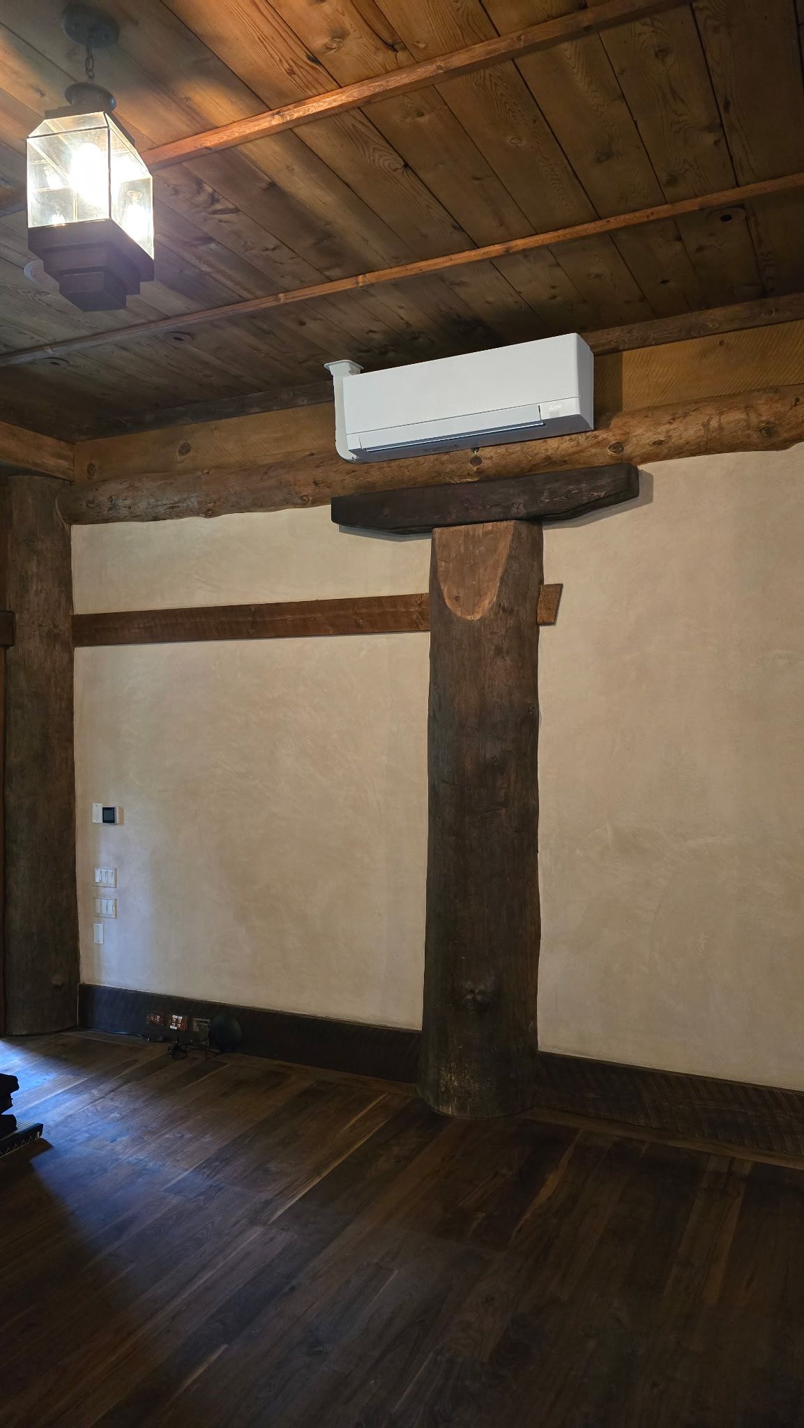 Rustic interior: Wooden pillar supports a platform with a light fixture above. Room has wooden floor and ceiling.