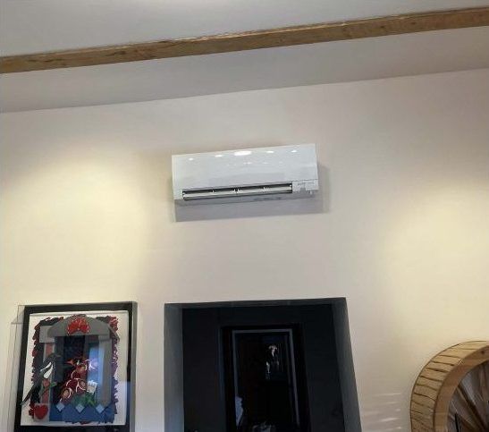 White air conditioner mounted on a beige wall above a doorway with a framed picture to the left.
