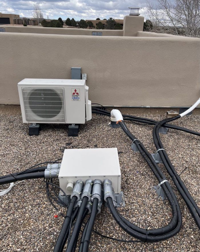 Mitsubishi air conditioning unit and junction box on a flat rooftop with black cables.