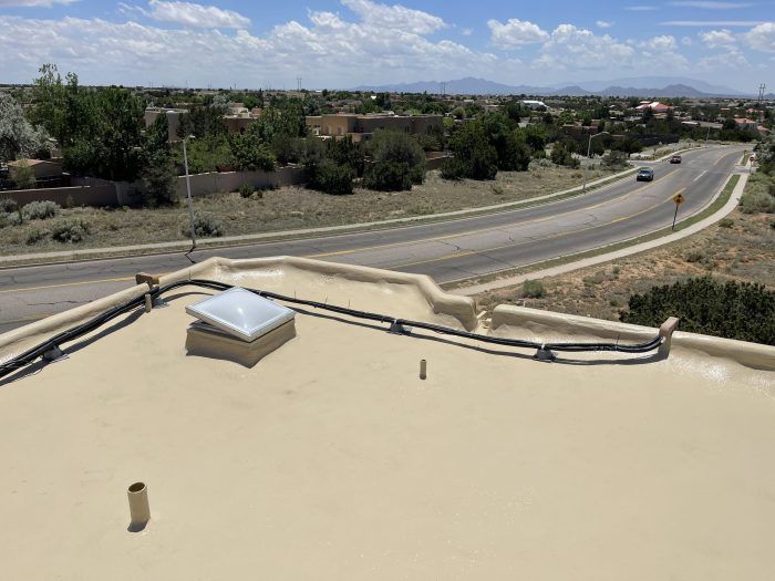 View from rooftop overlooking a road, homes, and distant mountains under a blue sky.