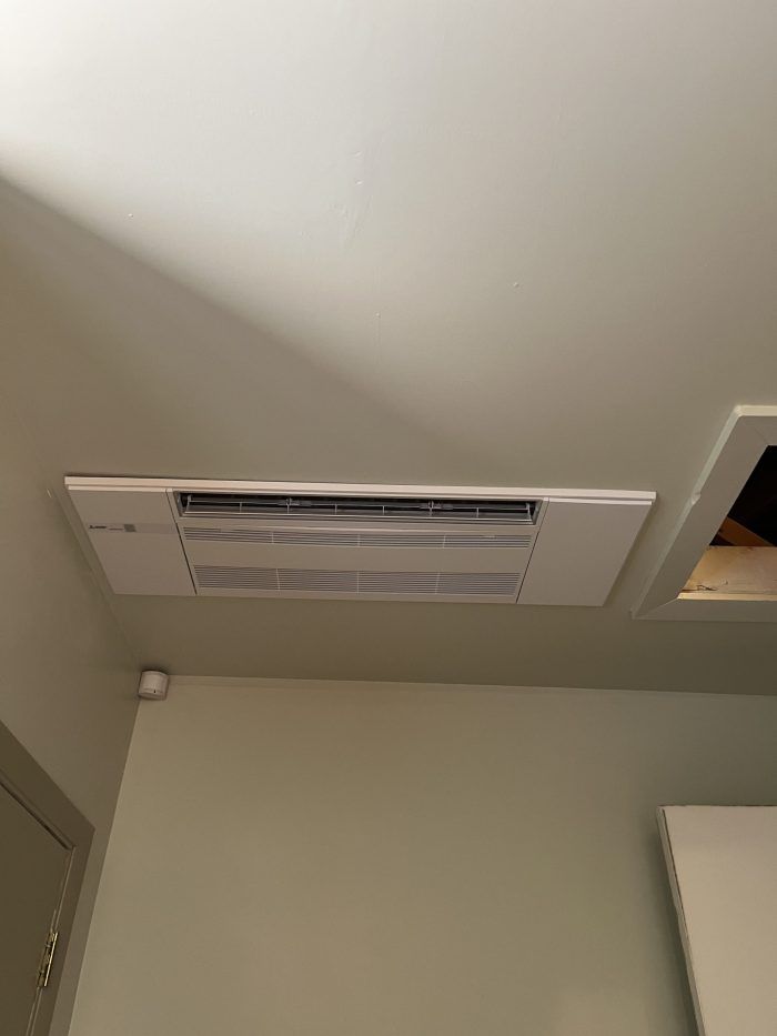 White ceiling-mounted HVAC unit with vents. Room has light green walls.