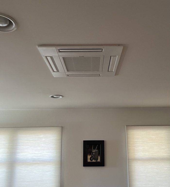 Ceiling-mounted HVAC unit, recessed lighting, and framed photo on a white wall; window blinds below.