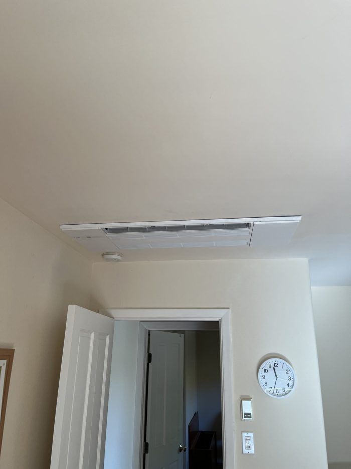 Ceiling with long vent, door, clock, and light switch on a cream-colored wall.