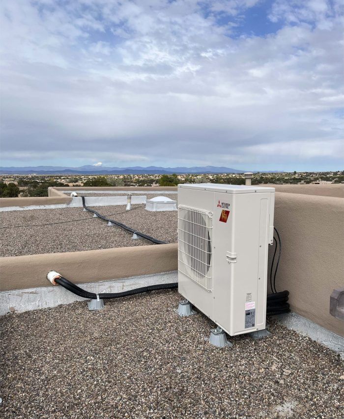 Rooftop air conditioning unit on a gravel surface, against a backdrop of a cloudy sky and distant landscape.