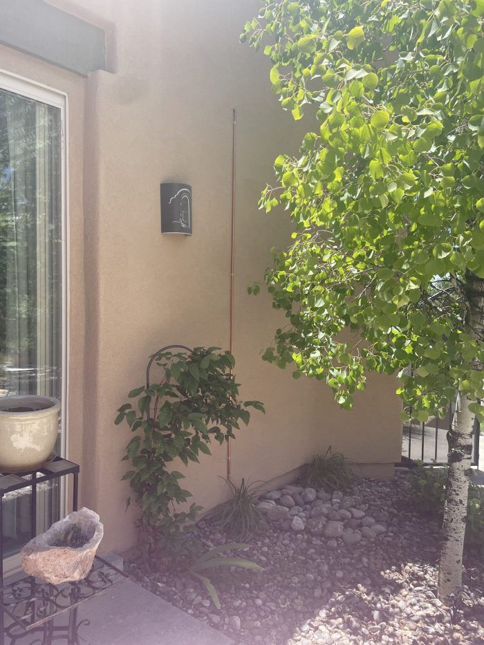 Tan stucco wall with outdoor light, small tree, and a lush green tree in front of a window.