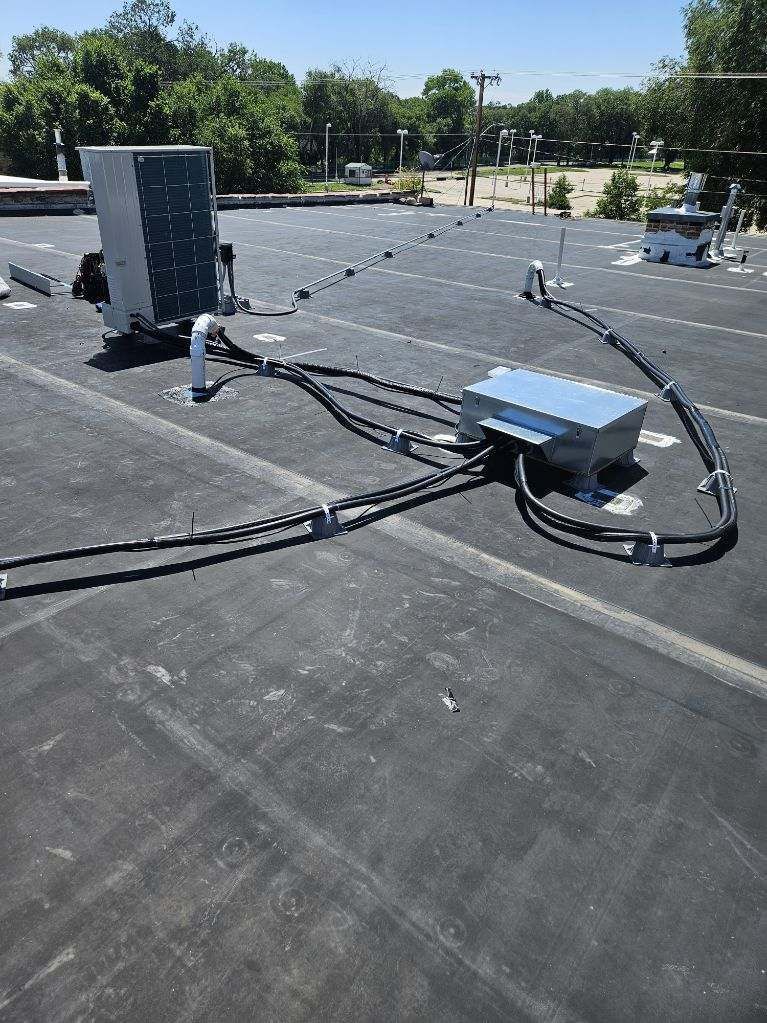Equipment on a black flat roof under a blue sky; includes a gray cabinet, boxes, and black cables.