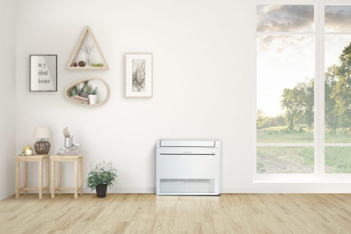 White air conditioner in a bright room with window overlooking a sunny landscape.