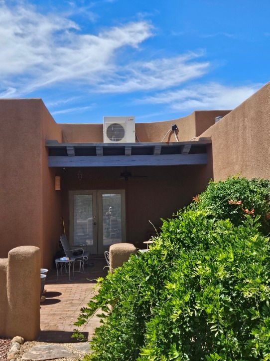 Courtyard with red brick patio, blue trim, and stucco walls. Air conditioning unit on roof.