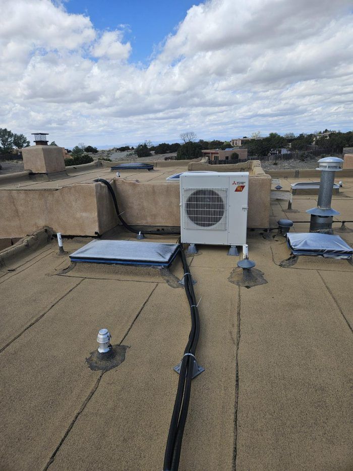 A rooftop with an air conditioning unit, vent pipes, and electrical conduit against a cloudy sky.