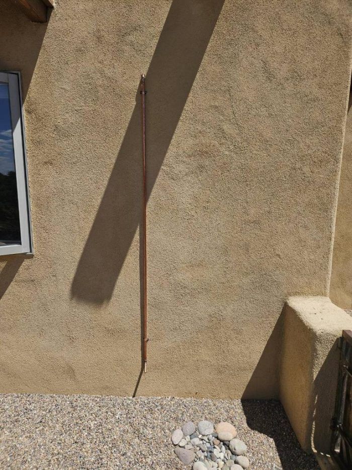 Copper grounding rod running down a stucco exterior wall. A shadow is cast diagonally across the wall.