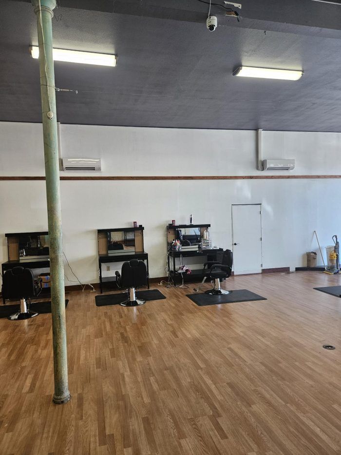 Interior of a hair salon with stations, chairs, and hardwood floors. White walls, black ceiling, and a support pole.