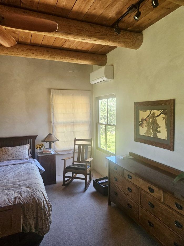 Bedroom with bed, dresser, rocking chair, window, and wood-beam ceiling.