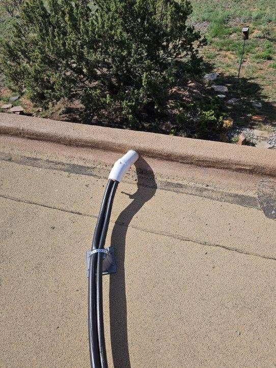 Black and white electrical cable secured to a tan wall, ending in a white cap. A tree is in the background.