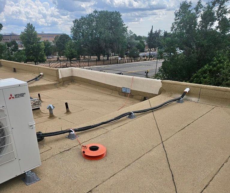 Rooftop with HVAC unit, cables, and orange coil. Trees and street in background.