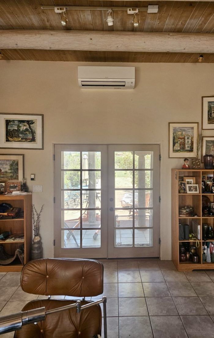 A room with French doors, an air conditioner, and various furnishings; light tan walls.