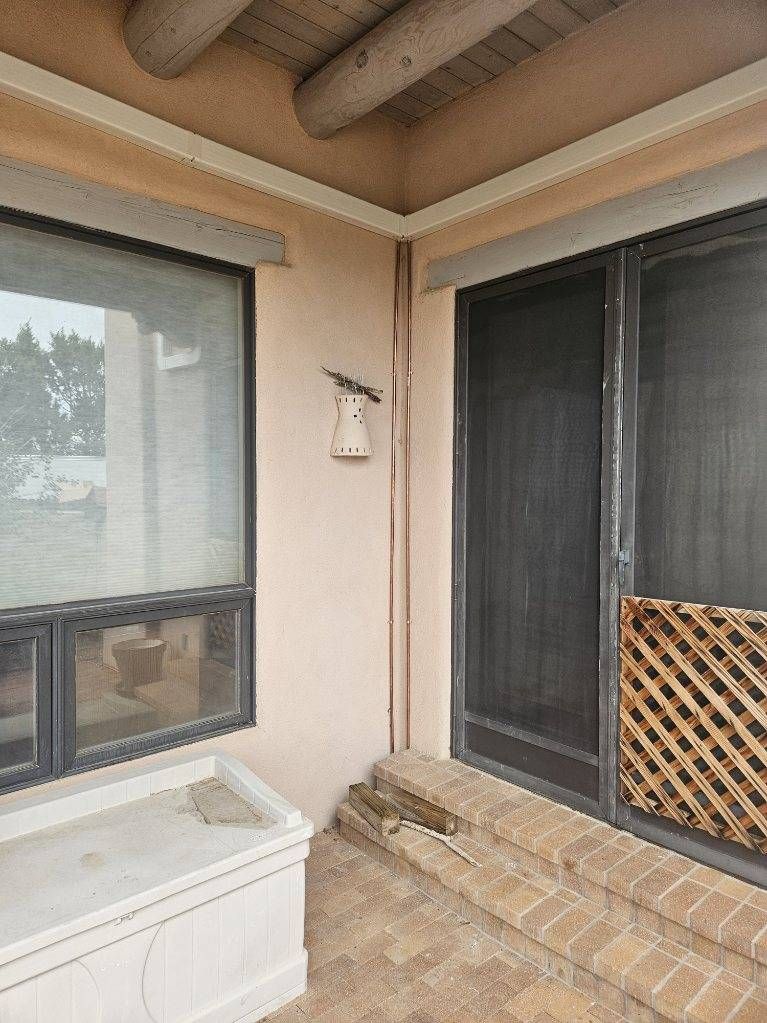 Corner of a building with a window and sliding screen door, beige walls, and brick steps.