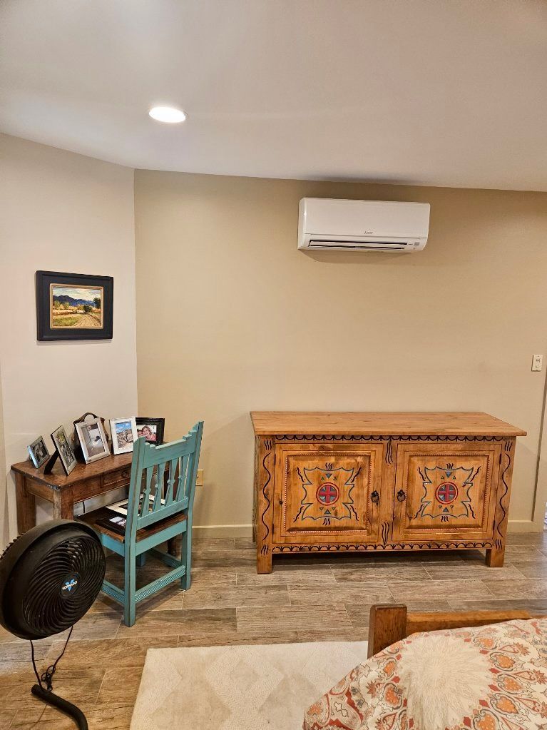 A room with a desk and blue chair, a decorative cabinet, and a wall-mounted air conditioner.