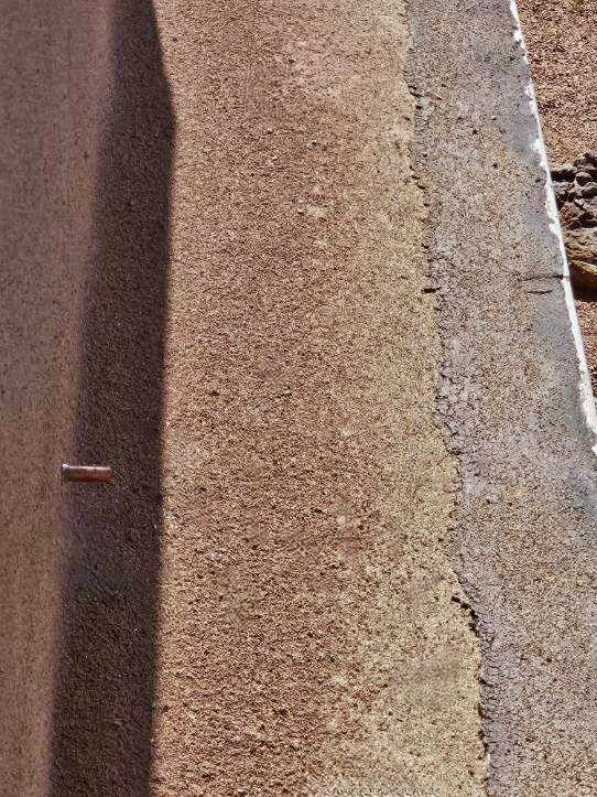 Close-up of a textured brown surface with a darker shadow, likely concrete or pavement.