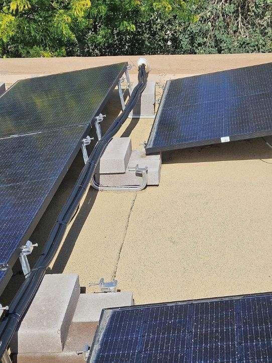 Solar panels mounted on a flat roof, held by concrete blocks and metal supports.