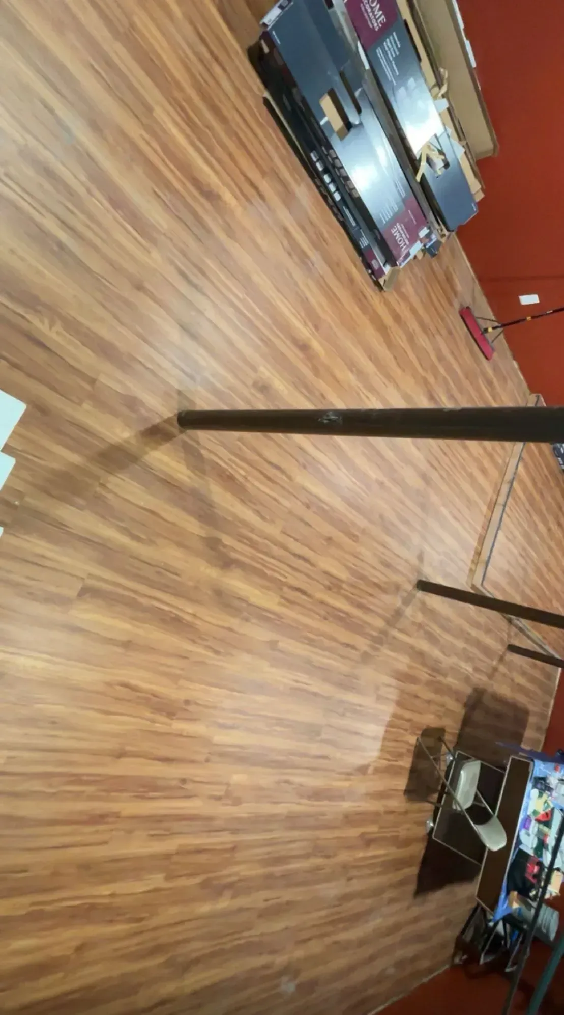 Wooden floorboards displayed in a store, with boxes stacked in the background, near a red wall.
