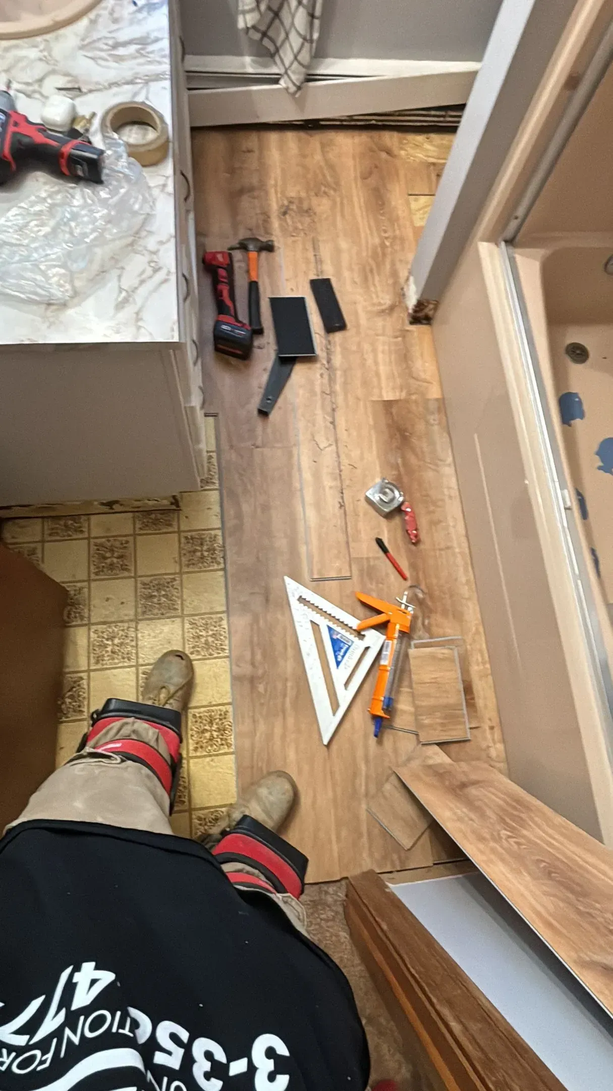 Bathroom flooring installation in progress with tools and materials scattered on the floor.