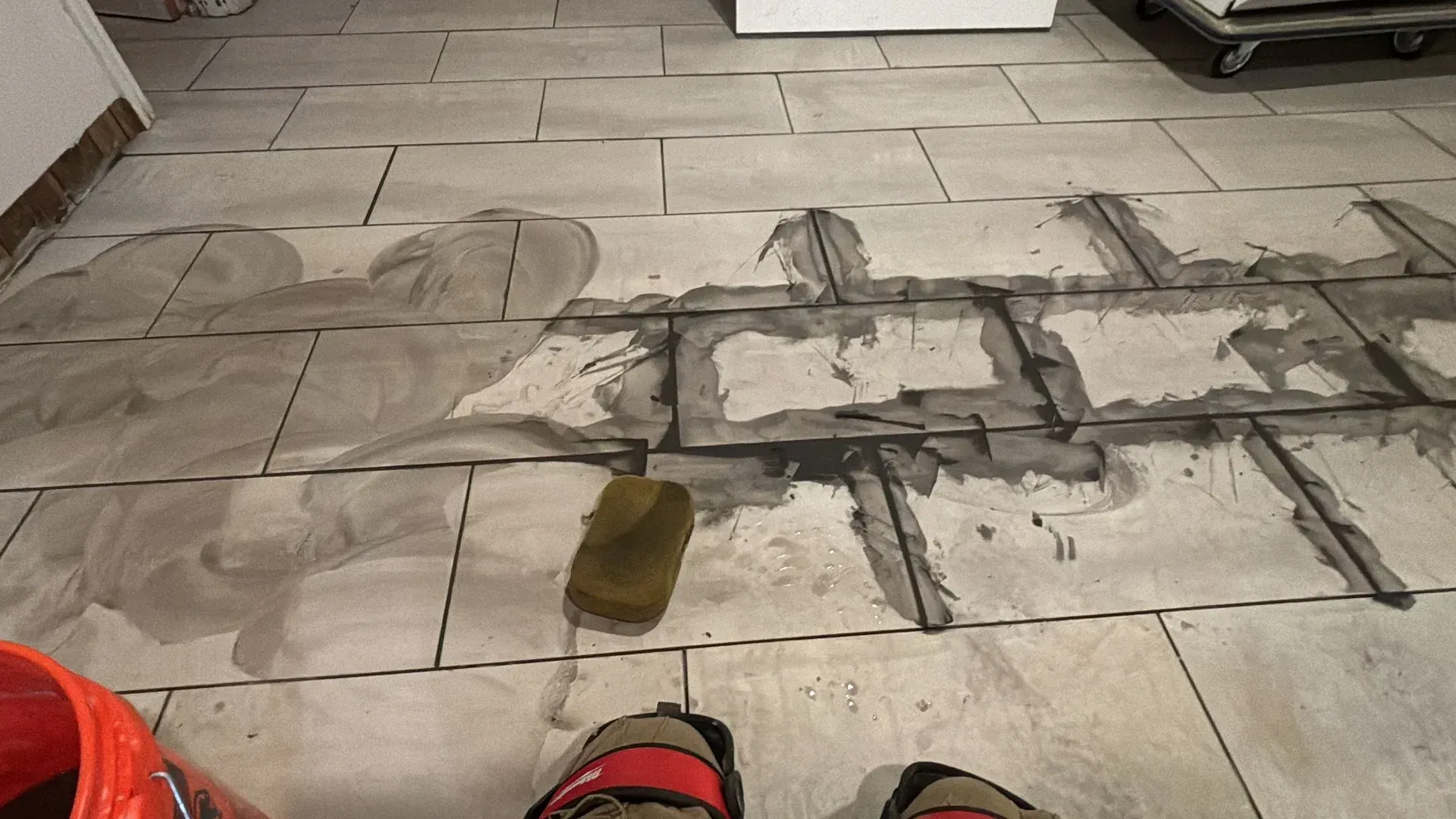 Tiled floor with grout application in progress. A sponge and bucket are visible.