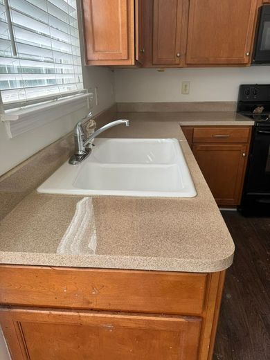 Kitchen with light brown countertops, white sink, wood cabinets, and a window with blinds.