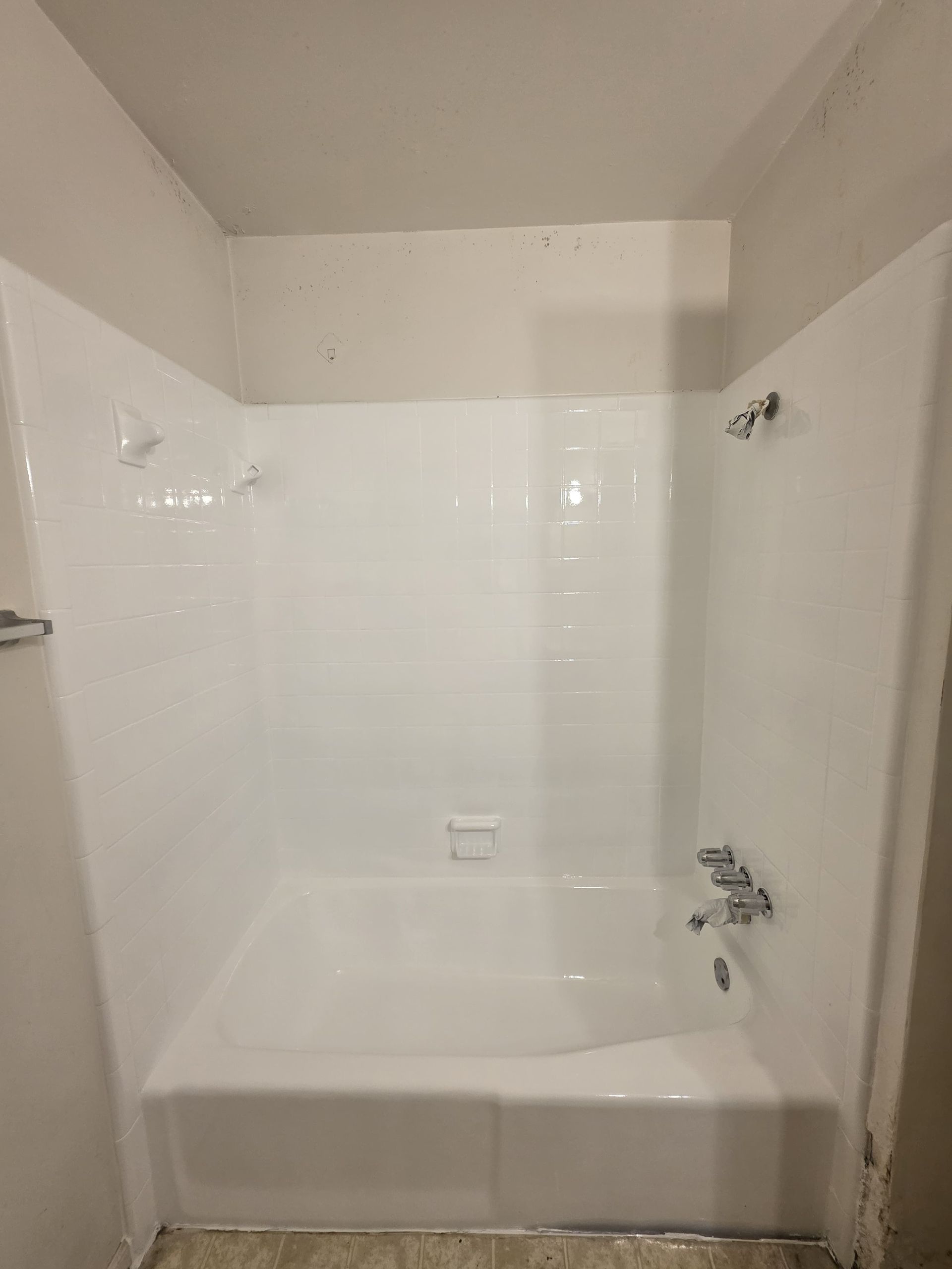 White shower stall with bathtub and fixtures; light grey walls.