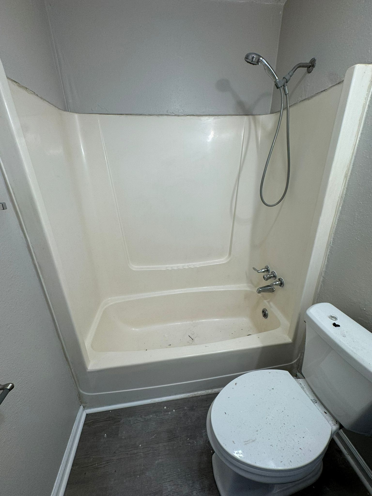A small bathroom with a white shower/tub, toilet, and gray walls.