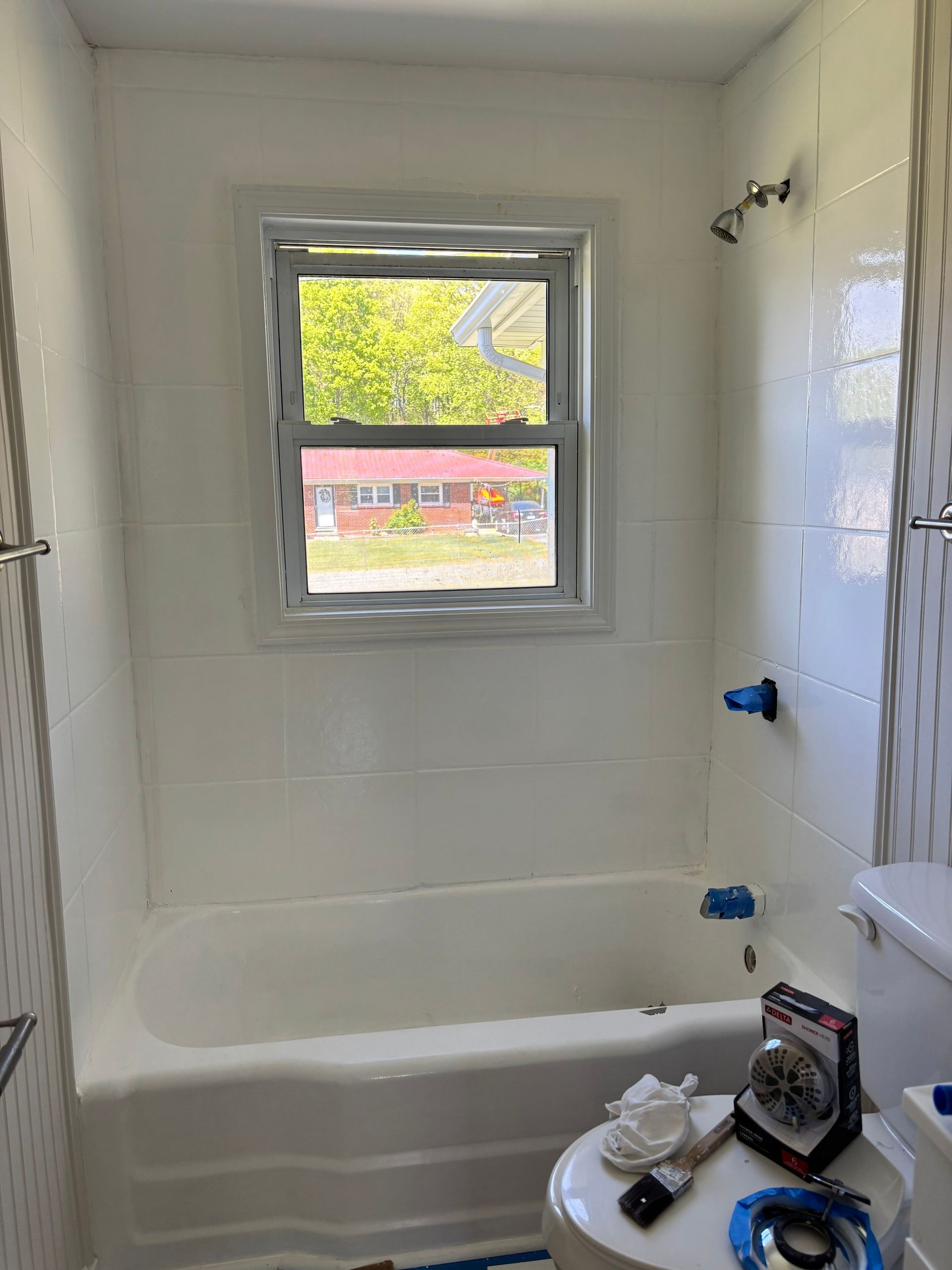 White bathroom with a window, bathtub, and toilet. The walls are tiled.