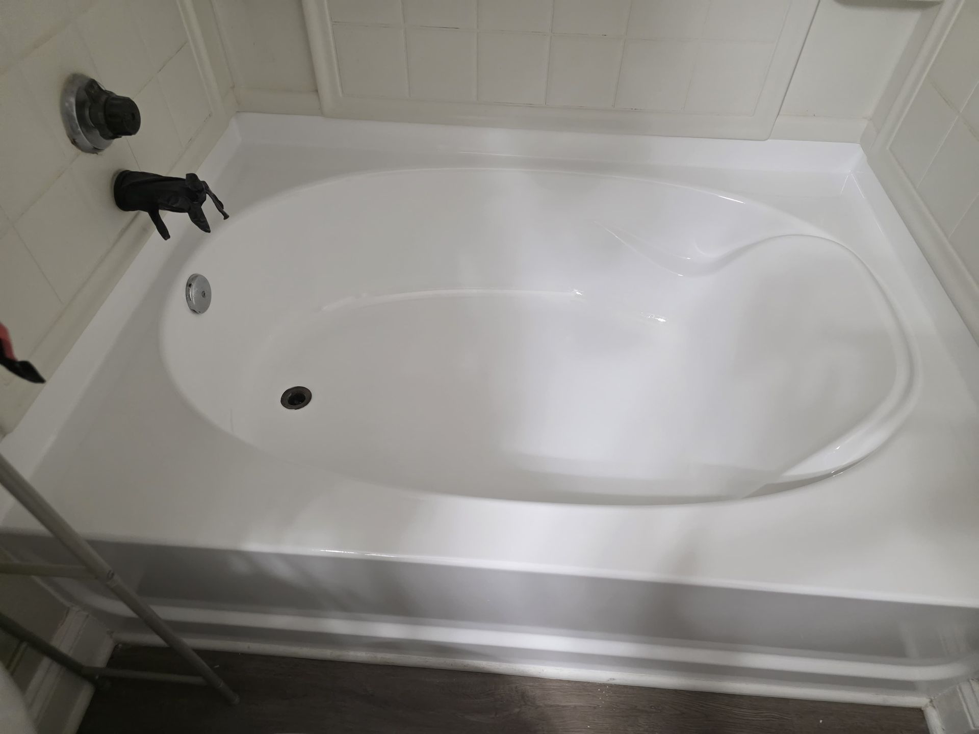 White oval bathtub with black faucet and drain in a white-tiled bathroom.