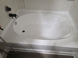 White bathtub with a curvy shape, set into a white surround in a bathroom.