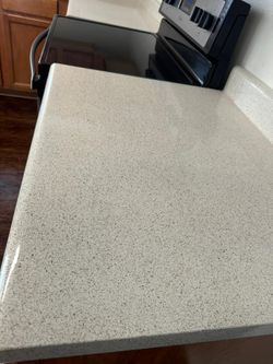 Beige speckled countertop next to a black electric stovetop, in a kitchen setting.