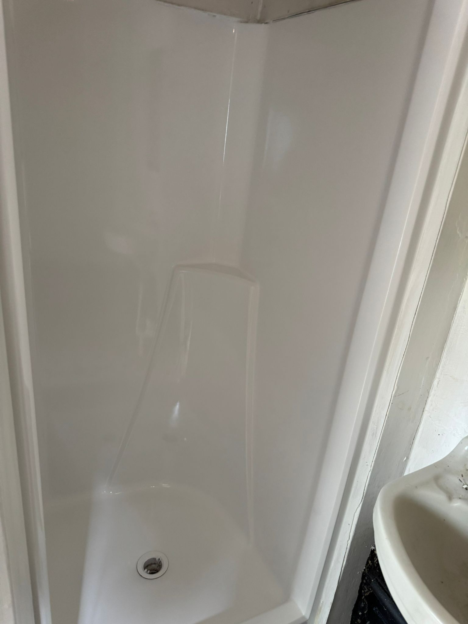 White, compact shower stall with a curved base and drain, next to a partially visible white sink.