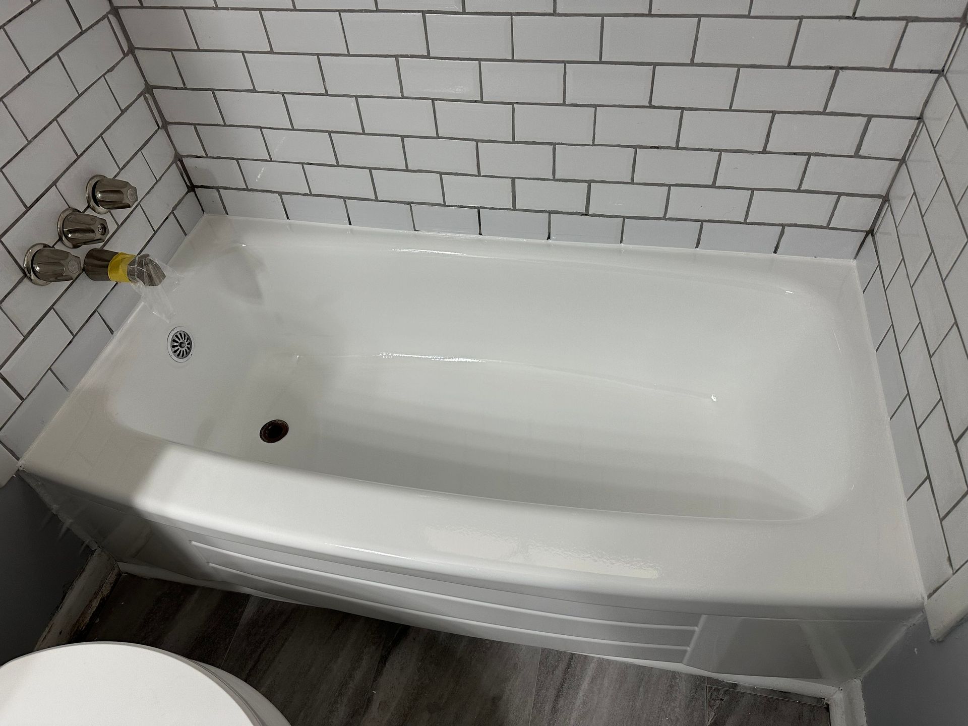 White bathtub with tiled walls, gray floor, and chrome fixtures.