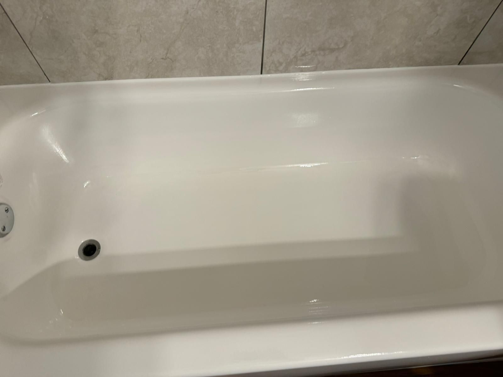 White bathtub, clean interior with drain and faucet fixture against beige tile wall.