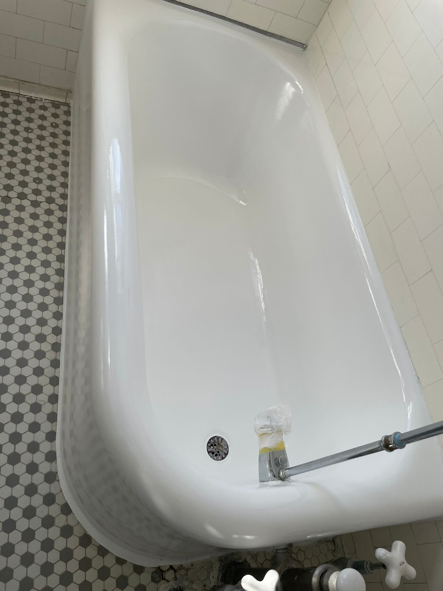 White bathtub in a tiled bathroom, with faucets and drain visible.