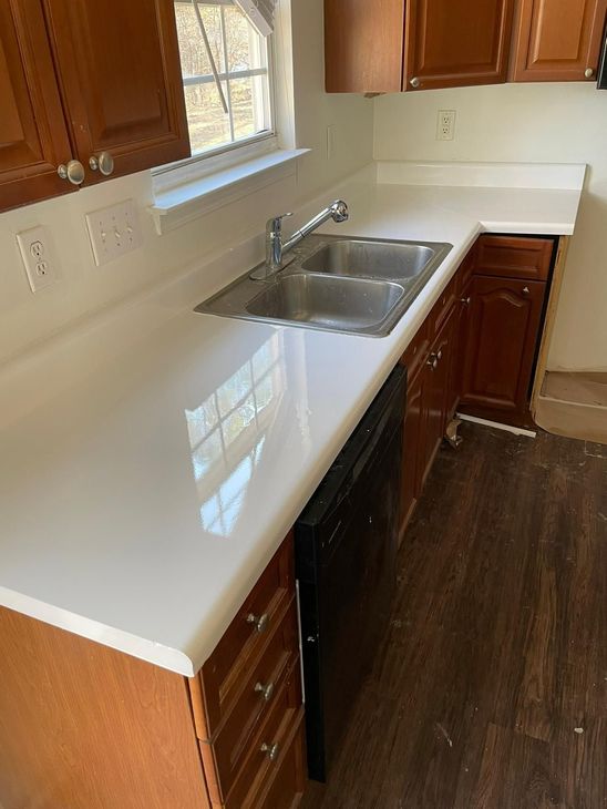 Kitchen with white countertop, stainless steel sink, and brown cabinets. Black dishwasher.