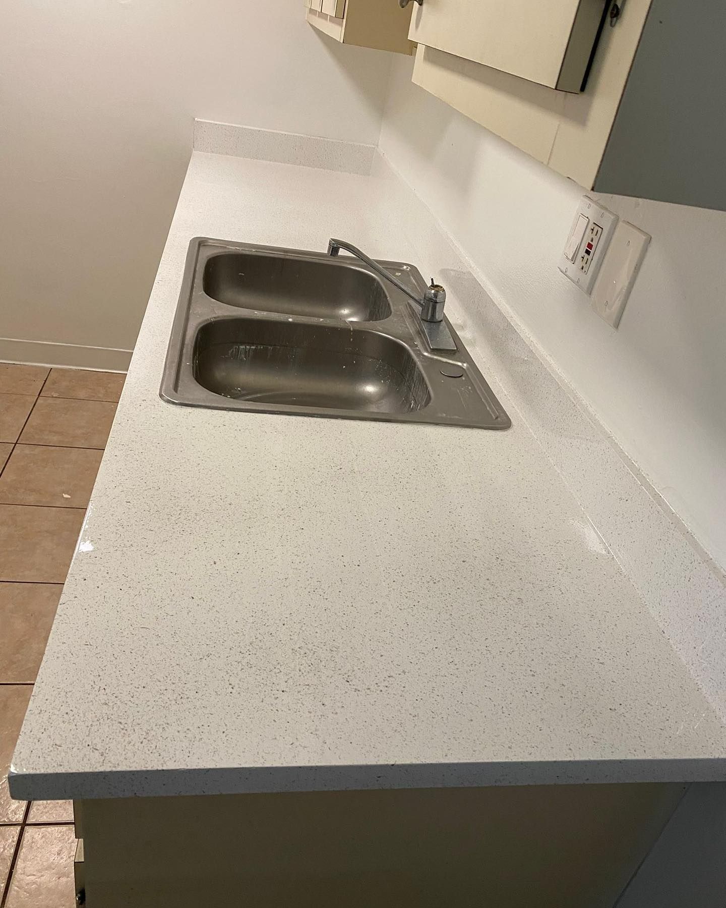 Stainless steel sink in a white speckled countertop.